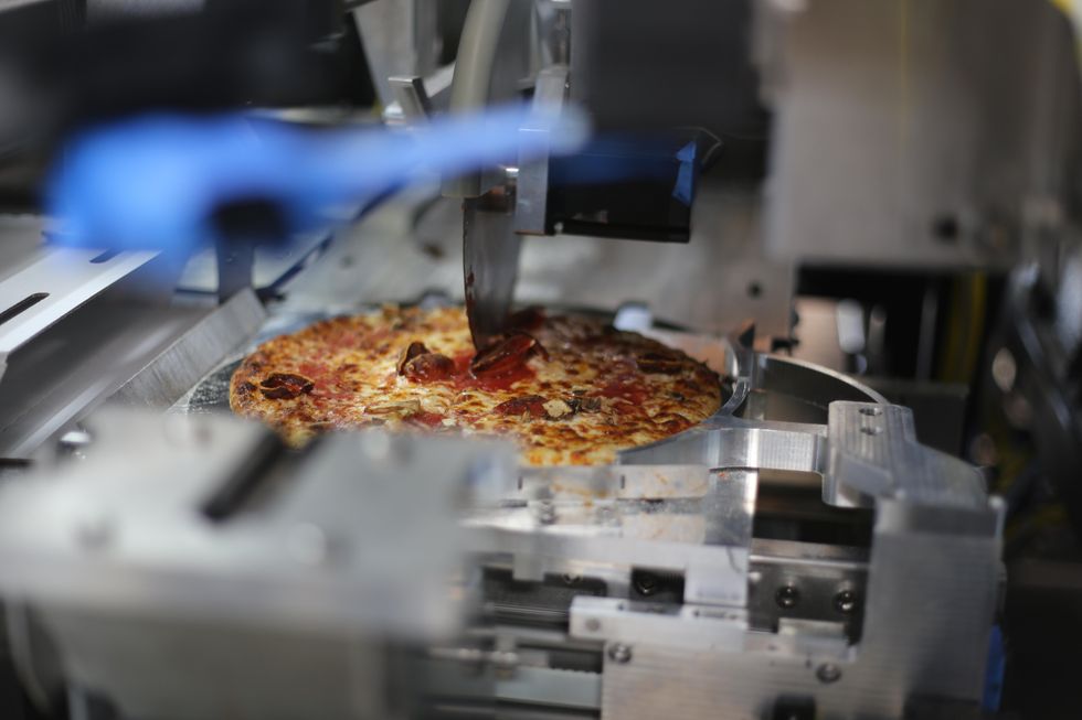 After cooking a pizza, the robotic Piestro machine cuts the pie into slices.