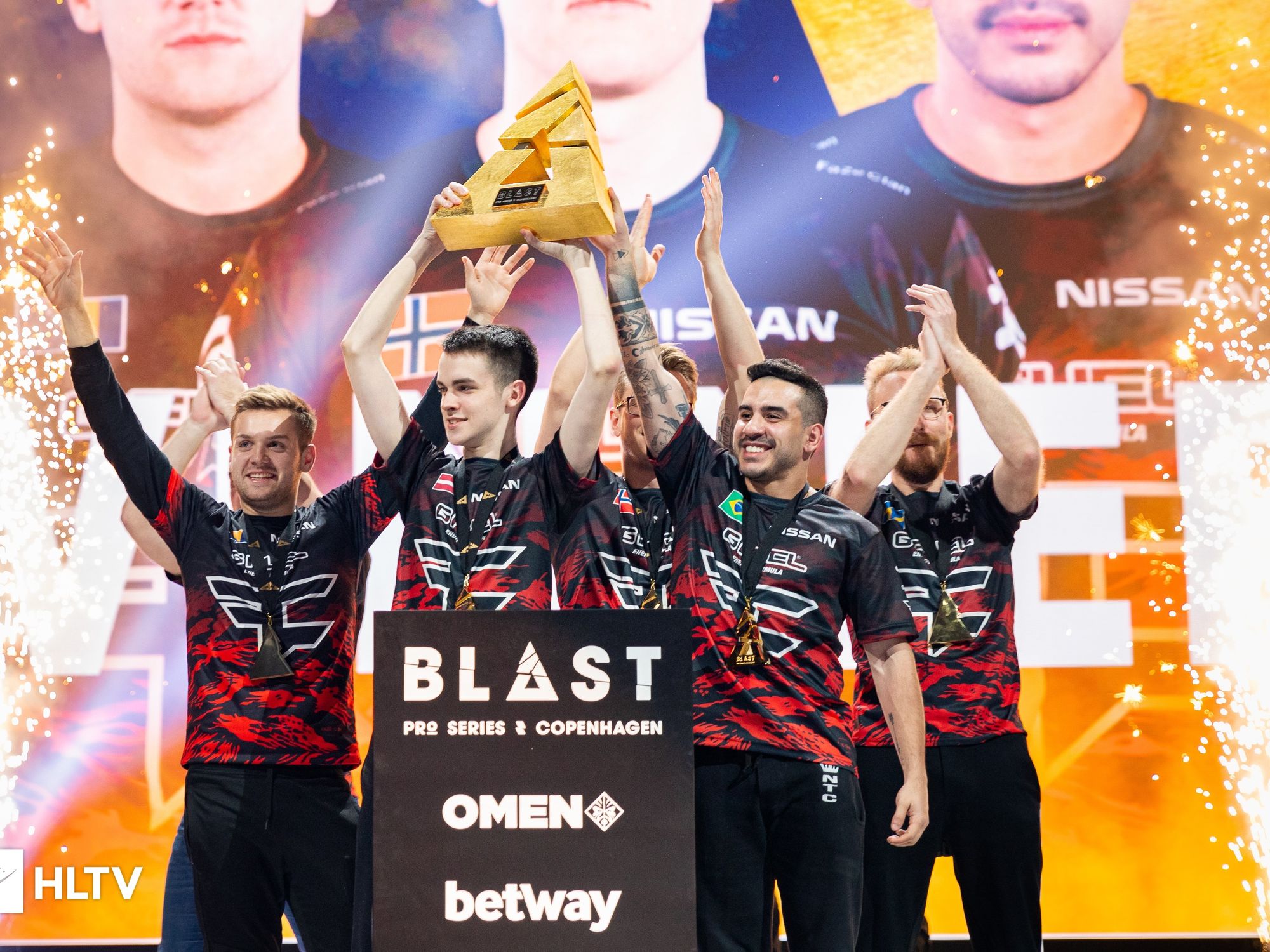 Gamers holding a trophy, fireworks on each side of the picture.
