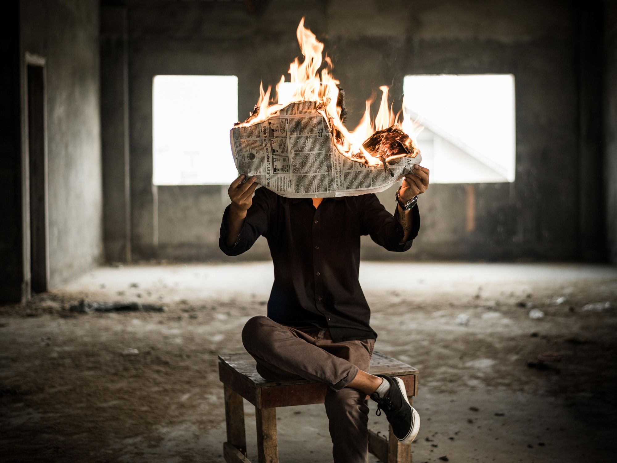 man sitting in chair with burning newspaper
