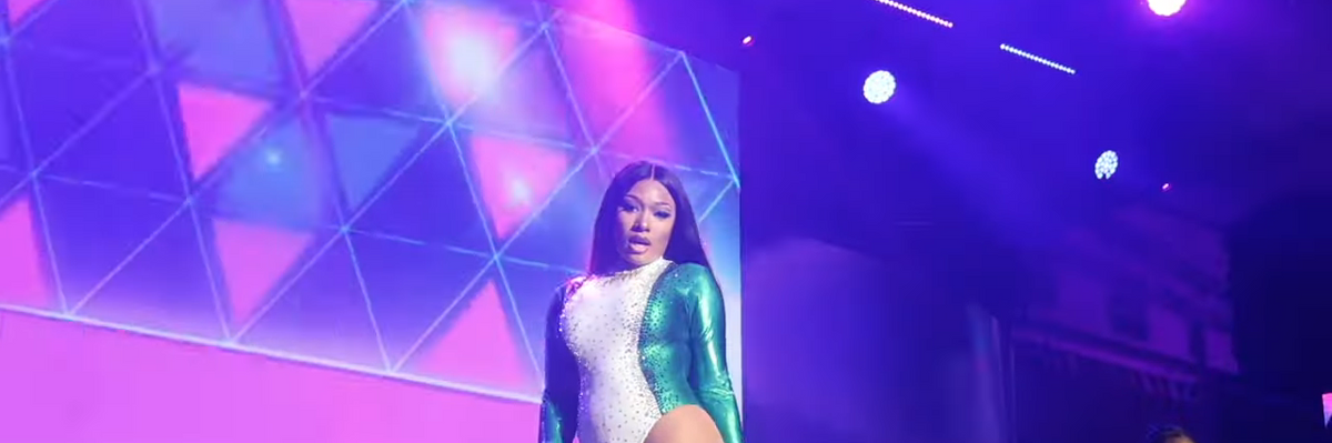 ​Megan Thee Stallion performing on stage in a blue and white leotard.