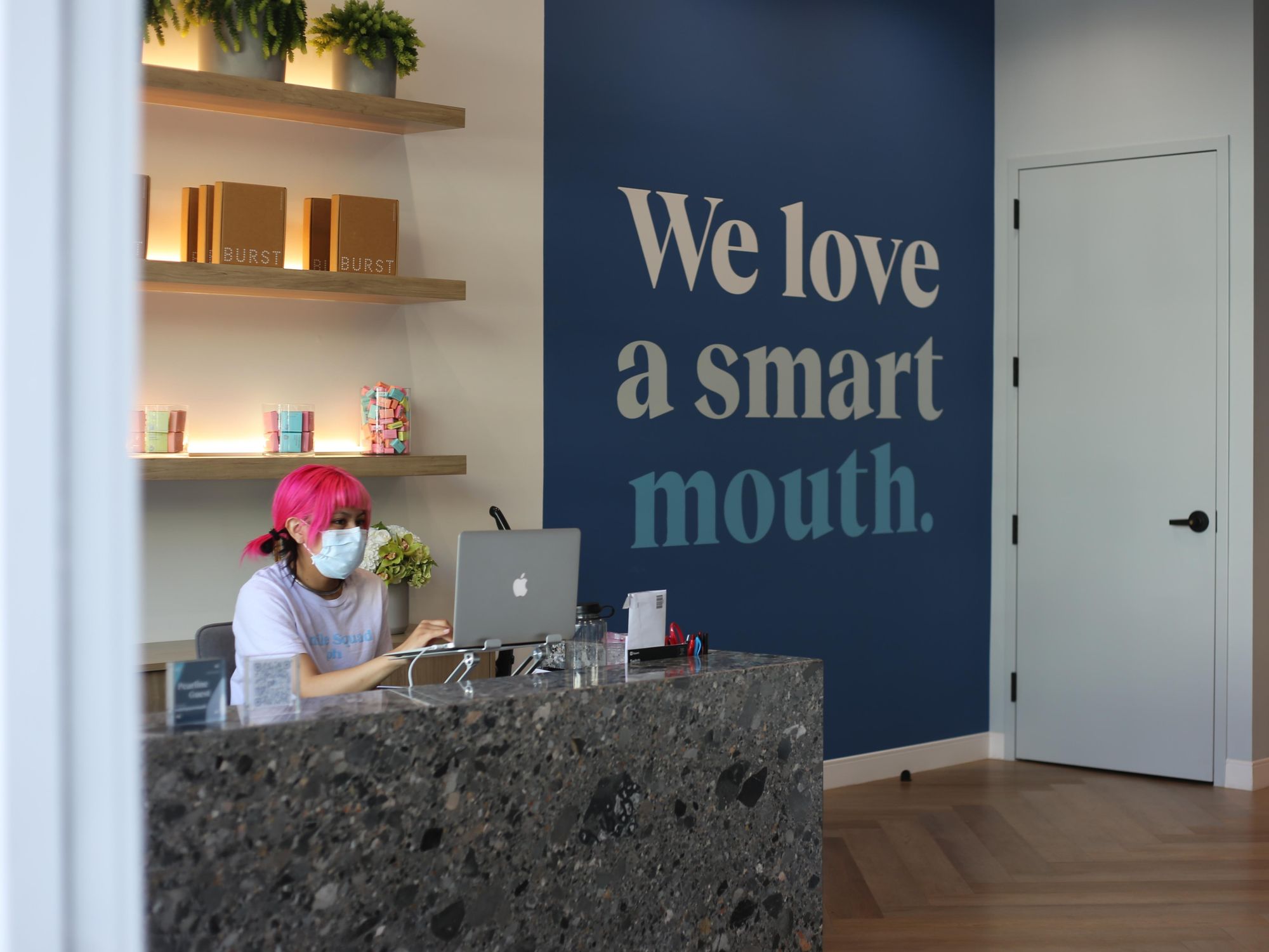 Pink-haired person with bangs working on a Macbook in the Pearline Health lobby.